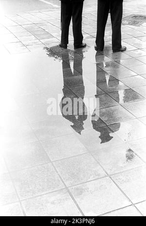 C'est un jour pluvieux à Stockholm Suède 1954. Les deux policiers sont visibles en pleine figure dans leur reflet dans la flaque de l'eau de pluie. Réf. 2A-1 Banque D'Images