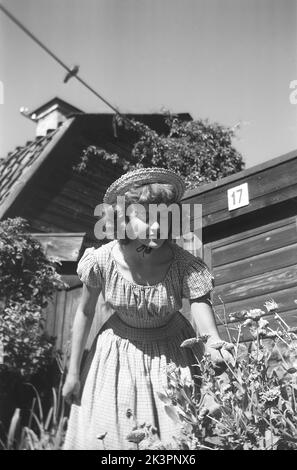 Dans le 1940s. Une jeune femme visite la ville de Stockholm, où elle est photographiée pour profiter du soleil et faire une pause dans la découverte de la ville. Elle porte une robe d'été et un chapeau. Une vieille maison historique est vue en arrière-plan dans la zone sud de la ville de Stockholm. Stockholm Suède 1949. Kristoffersson réf. AO31-1 Banque D'Images