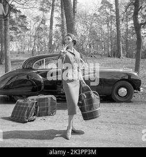 Dans le 1950s. Une jeune femme dans une tenue assortie de veste et de jupe, typiquement 1950s. Elle se tient devant une voiture aux courbes magnifiques avec trois sacs et des bagages assortis. Suède 1956 Banque D'Images