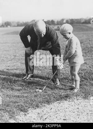 Golf dans le 1930s. Une jolie scène au parcours Woodcote où Derick Paine, cinq ans, est conseillé par son père sur la façon de tenir le club de golf. 28 septembre 1934. Le Woodcote Park Golf Club a été fondé en 1912 et est situé entre Purley et Coulsdon à Surrey. Banque D'Images