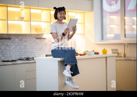 Fille avec un gadget posant pour l'appareil photo dans la cuisine Banque D'Images