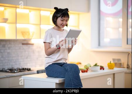 Jeune femme avec un gadget assis dans la cuisine Banque D'Images