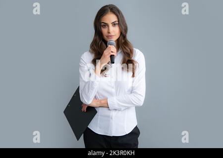 Jeune femme journaliste ou femme d'affaires avec microphone et presse-papiers sur fond gris. Banque D'Images