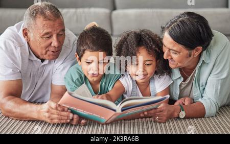 La famille, le livre et les enfants en train de lire la croissance à la maison avec les grands-parents sur le plancher. Enfants, personnes âgées et heureux regardant des livres, histoire Banque D'Images