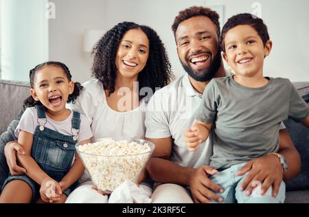 Aimez, rigolez et regardez la télévision ou un film avec une famille heureuse en train de manger du pop-corn, en s'amusant et en souriant ensemble à la maison. Portrait des parents latino et Banque D'Images