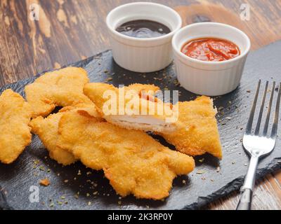 De savoureuses lanières de poulet avec sauce barbecue et sauce tomate sur un plateau en pierre noire Banque D'Images