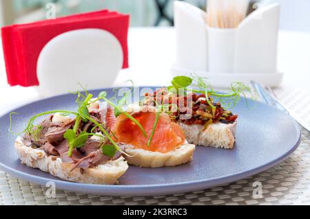savoureux assortiment de bruschetta sur une assiette : saumon, bœuf, légumes. Mise au point sélectionnée. Banque D'Images