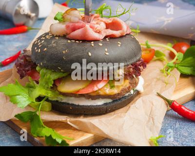 Hamburger noir savoureux avec escalope de poulet, bacon, fromage, concombres et tomates Banque D'Images