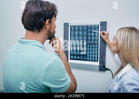 Médecin pratiquant avec le patient mâle regardant l'IRM du cerveau sur le nématoscope dans le bureau du médecin. Scanner, IRM de la tête, résultat radiologique Banque D'Images