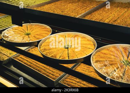 Vue en perspective gros plan de grandes assiettes de baklava ou de baklawa sucrées arabes sur les étagères de la fenêtre du magasin de rue Banque D'Images