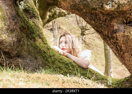 une fille dans une forêt qui se trouve sur un arbre, se reposer dans la nature. en arrière-plan, silhouettes d'arbres floues. Santé mentale. Émotion positive. Banque D'Images