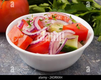 salade de légumes savoureuse de concombres tomates et oignons dans un bol blanc. Gros plan Banque D'Images