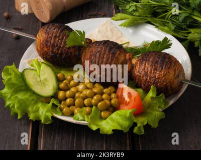 pommes de terre savoureuses sur des charbons sur une brochette, décorées de petits pois verts Banque D'Images