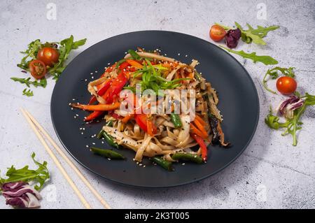 Nouilles udon savoureuses avec légumes sur une assiette noire. Cuisine asiatique Banque D'Images