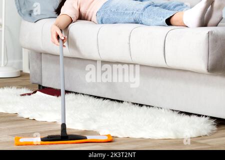 Femme se reposant sur le canapé après avoir nettoyé un sol Banque D'Images