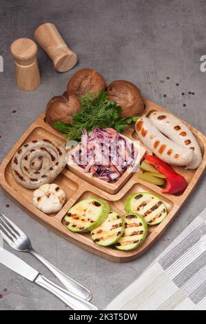 assiette en bois avec saucisses grillées, courgettes, chou rouge et petits pains Banque D'Images