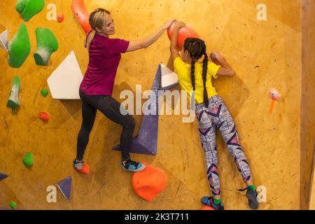 Les jeunes femmes d'aider l'instructeur d'escalade grimper garçon mur artificiel Banque D'Images