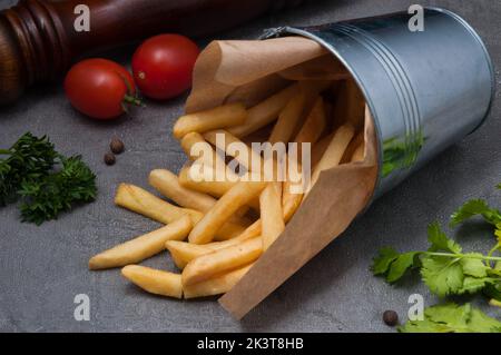 frites savoureuses dans un seau en métal sur fond gris Banque D'Images