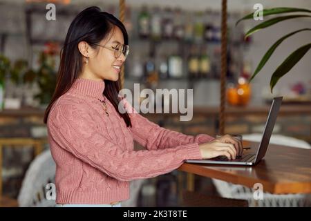 Une étudiante asiatique fait son travail sur un ordinateur portable tout en étant assise dans un café. Banque D'Images