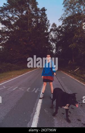 Femme voyageur avec chien marchant le long de la route asphaltée près de la forêt de hêtres le jour d'automne brumeux en Espagne Banque D'Images