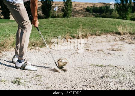 Vue latérale au niveau du sol de la récolte anonyme athlète masculin dans les chaussures de golf frapper balle avec putter dans la zone de sable dangereux du terrain Banque D'Images