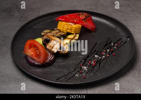 de savoureux légumes grillés sur une assiette foncée, garnis de poivre et de sel Banque D'Images