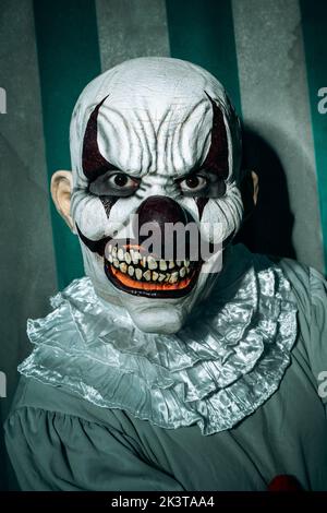 gros plan d'un clown maléfique caillé, portant un costume gris avec une ruff blanche, se trouve à l'observateur avec un sourire effrayant, devant un sale an Banque D'Images