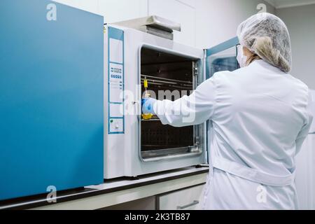 Vue arrière scientifique portant des gants, un masque et un capuchon travaillant en laboratoire Banque D'Images