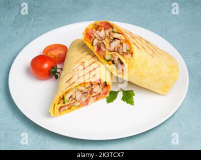 shawarma savoureux avec poulet et légumes dans du pain pita au fromage sur fond bleu. Banque D'Images