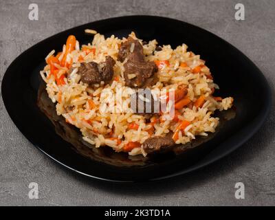 Pilaf ouzbek traditionnel savoureux sur une assiette noire sur fond gris Banque D'Images