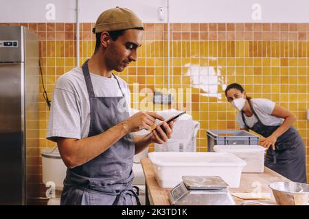 Jeune homme propriétaire d'entreprise utilisant le téléphone mobile et de faire l'ordre au fournisseur tout en travaillant avec la femme dans la boulangerie Banque D'Images
