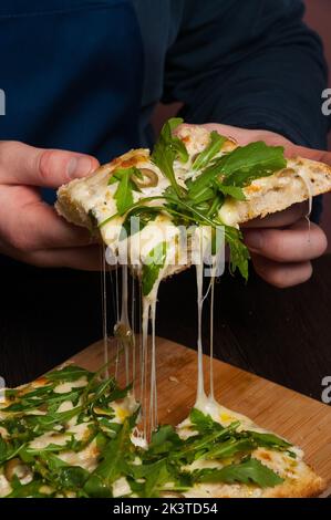 un homme prend une tranche de pizza savoureuse. le fromage s'étire Banque D'Images