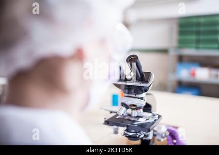 vue arrière d'une femme scientifique anonyme regardant au microscope en laboratoire Banque D'Images