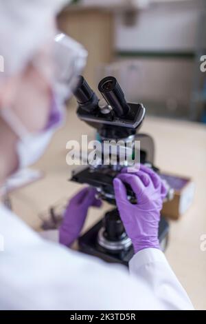 vue arrière d'une femme scientifique anonyme regardant au microscope en laboratoire Banque D'Images