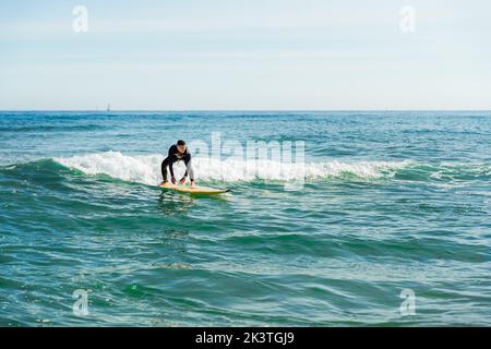 Pleine longueur de jeune surfeur mâle en combinaison avec planche de surf sur l'eau de mer ondulée tout en pratiquant le sport extrême sur la plage Banque D'Images