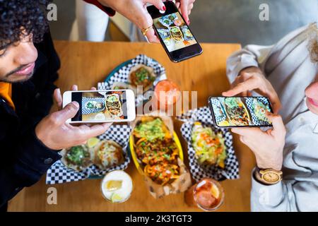 Vue du haut crop anonyme amis prenant des photos de délicieux aliments sur les smartphones tout en se rassemblant à table dans le restaurant Banque D'Images