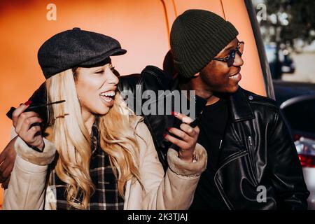 Beau gars afro-américain souriant et embrassant belle femme riant avec mascara tout en se tenant dans la rue ensemble Banque D'Images