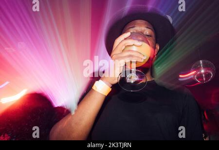 Petit angle de gars afro-américains sirotant un cocktail d'alcool sous un éclairage coloré pendant la fête à la discothèque Banque D'Images