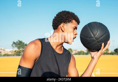 Vue latérale du joueur afro-américain en uniforme regardant la caméra avec le ballon dans la journée lumineuse sur le terrain de jeu Banque D'Images