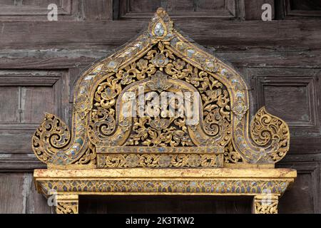 Gros plan d'un ancien panneau de sculpture en bois doré au-dessus de la fenêtre du monument historique Wat Phan Tao, façade du temple bouddhiste, Chiang Mai, Thaïlande Banque D'Images