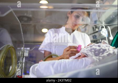 Travailleur médical qui allaite un bébé prématuré avec des tubes fixés dans un incubateur moderne pendant son travail à l'hôpital Banque D'Images