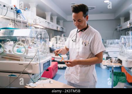 Pédiatre en seringue de remplissage uniforme blanche avec vaccin à injecter en chambre avec incubateurs pour nouveau-nés à l'hôpital Banque D'Images