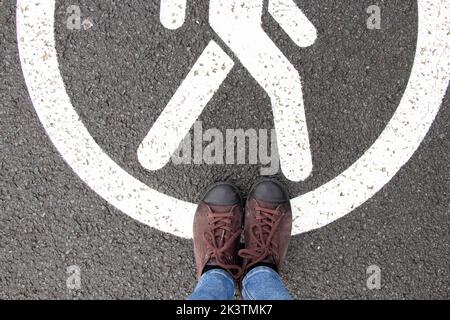 Le panneau piéton est dessiné sur la chaussée et à côté il y a des jambes femelles dans les baskets, une route piétonne et des jambes Banque D'Images