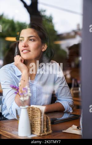 Photo prise à travers la fenêtre de la femme latino-américaine profondément dans la pensée assis au café Banque D'Images