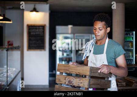 Jeune travailleur sérieux d'épicerie d'Amérique latine tenant une caisse en bois Banque D'Images