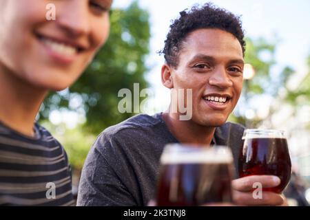 Portrait d'un jeune homme afro-américain heureux souriant à la caméra tout en tenant un verre de bière Banque D'Images