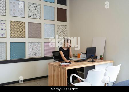 Vue grand angle d'une femme entrepreneure de design d'intérieur qui parle au téléphone à son bureau Banque D'Images