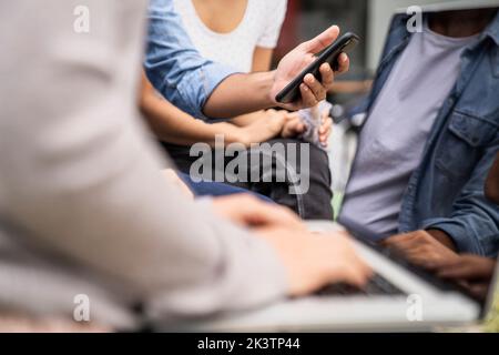 Gros plan sur les mains de jeunes travailleurs indépendants et de sous-traitants indépendants utilisant la technologie mobile pour se connecter au réseau tout en travaillant à l'extérieur Banque D'Images