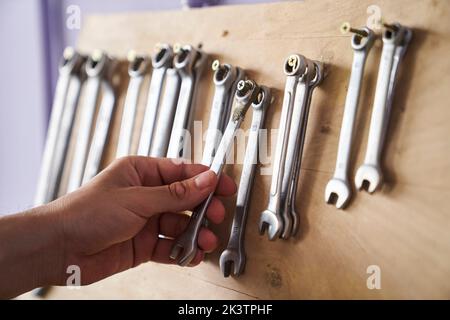 Gros plan de la main prenant une clé mixte d'un support mural Banque D'Images