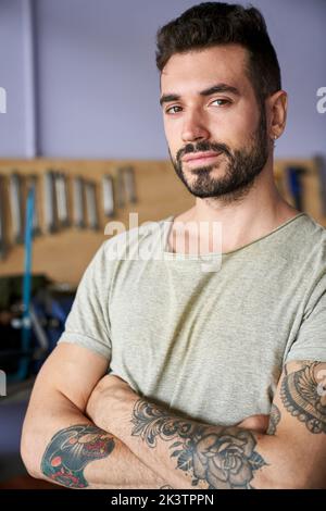 Portrait moyen d'un propriétaire d'atelier barbu debout dans son atelier devant ses outils Banque D'Images